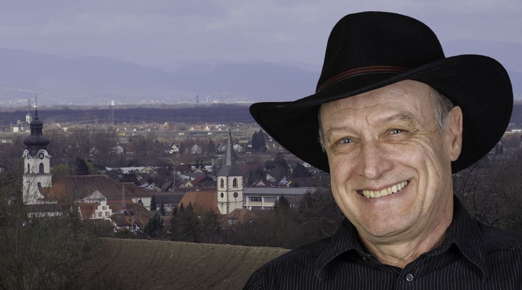 Foto-Collage: Mann mit Hut vor Dorf-Panorama